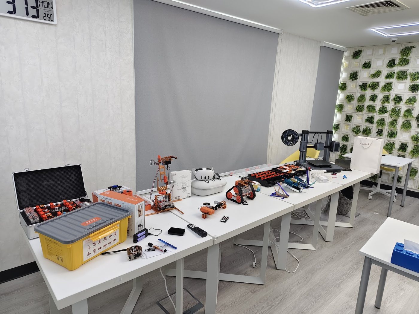 Engineering lab with robot kits, a robot arm, tracked robots and a 3D printer laid out on tables